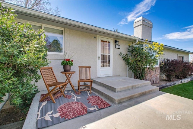 view of exterior entry featuring a chimney and stucco siding