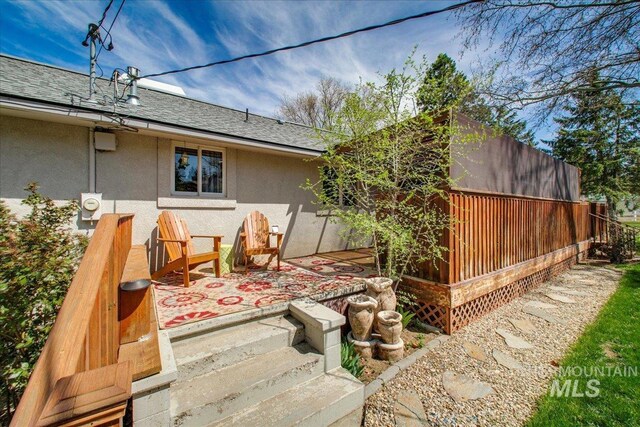 rear view of house with a shingled roof, stucco siding, and fence