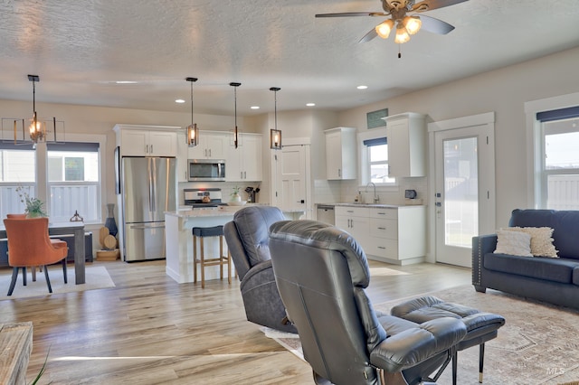 living room featuring a textured ceiling, a wealth of natural light, light hardwood / wood-style floors, and ceiling fan with notable chandelier