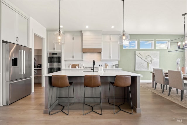 5222 S Montague Way, Meridian, ID 83642 - kitchen featuring appliances with stainless steel finishes, light countertops, custom exhaust hood, light wood-style floors, and a center island with sink