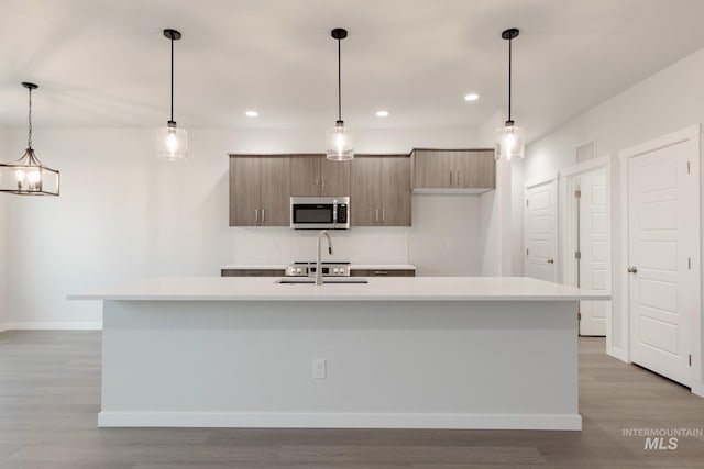 kitchen featuring sink, a kitchen island with sink, decorative backsplash, and hanging light fixtures