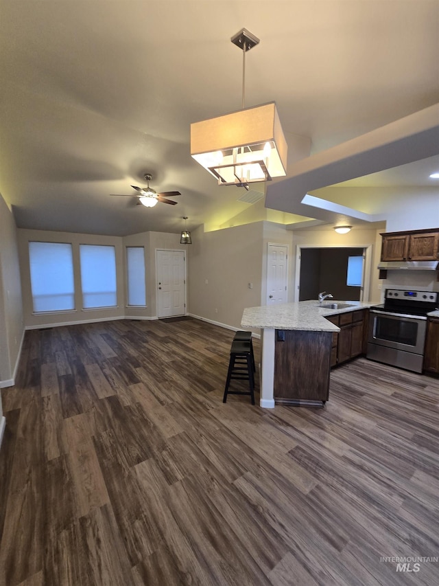 kitchen with dark wood finished floors, stainless steel electric range oven, open floor plan, a kitchen breakfast bar, and a sink