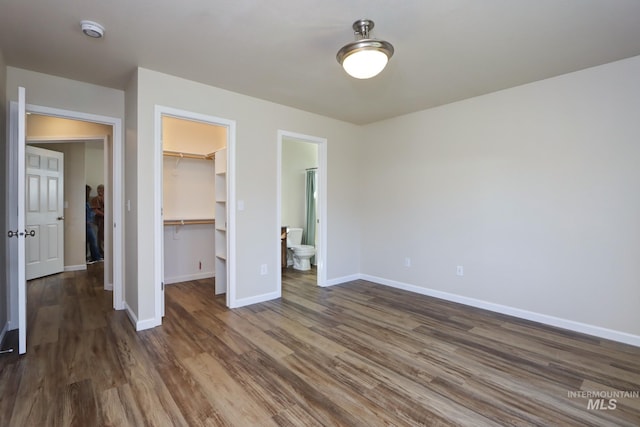 unfurnished bedroom with connected bathroom, baseboards, a closet, a walk in closet, and dark wood finished floors