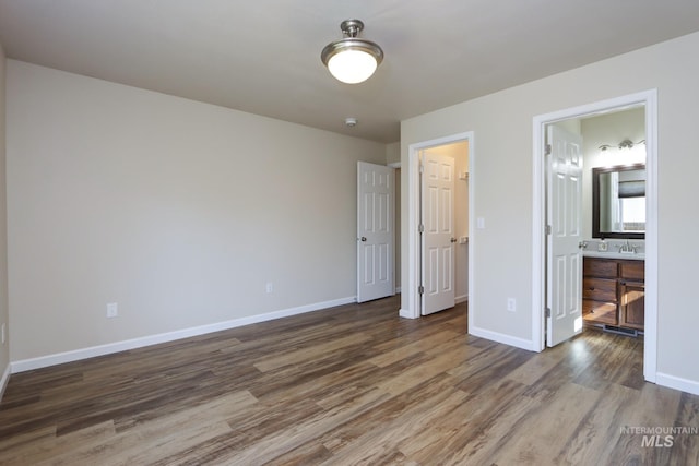 unfurnished bedroom featuring ensuite bath, baseboards, and wood finished floors