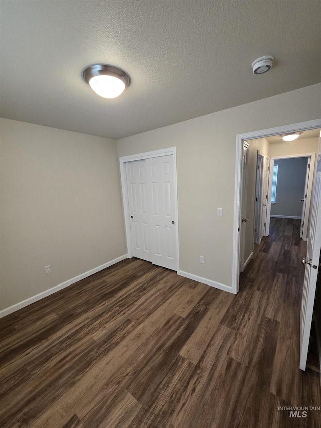 unfurnished bedroom featuring dark wood-type flooring, a closet, a textured ceiling, and baseboards