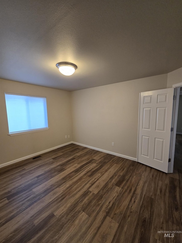 empty room with visible vents, a textured ceiling, baseboards, and dark wood-type flooring