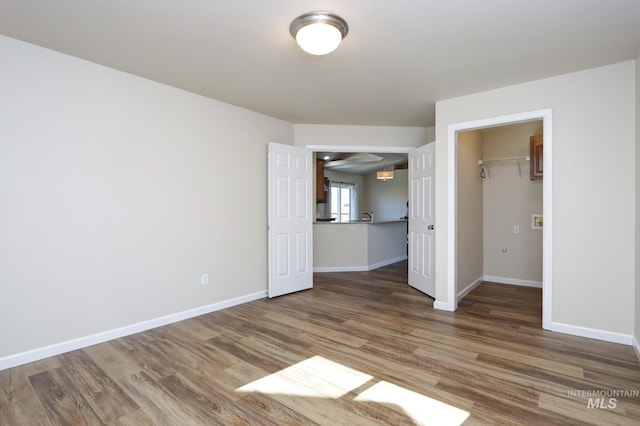 unfurnished bedroom with a spacious closet, a closet, wood finished floors, and baseboards