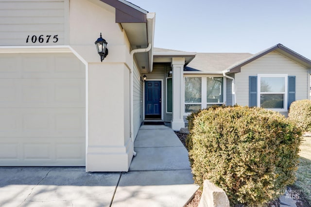 view of exterior entry with a garage, roof with shingles, and stucco siding