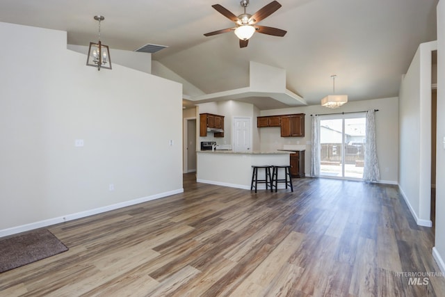 unfurnished living room with ceiling fan with notable chandelier, wood finished floors, visible vents, and baseboards