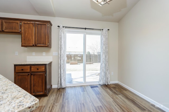 kitchen with light stone countertops, light wood finished floors, baseboards, and visible vents