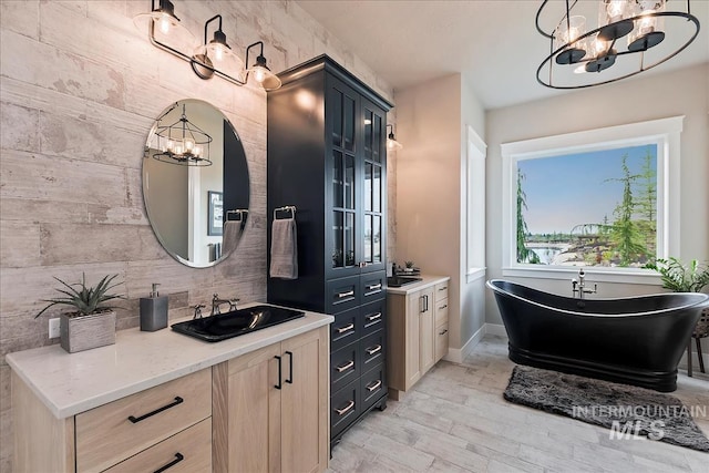 bathroom with baseboards, a freestanding tub, a notable chandelier, vanity, and wood finished floors