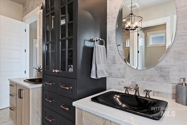bathroom featuring visible vents, decorative backsplash, a notable chandelier, and vanity