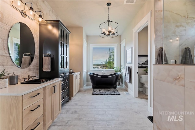 bathroom with an inviting chandelier, a freestanding tub, vanity, toilet, and wood finished floors