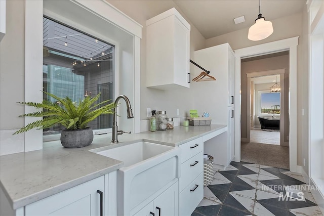 interior space with white cabinetry, light stone countertops, decorative light fixtures, dark carpet, and a sink