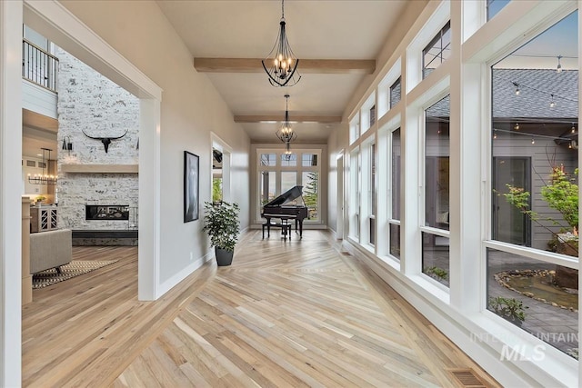 hallway featuring a notable chandelier, baseboards, visible vents, beam ceiling, and wood finished floors