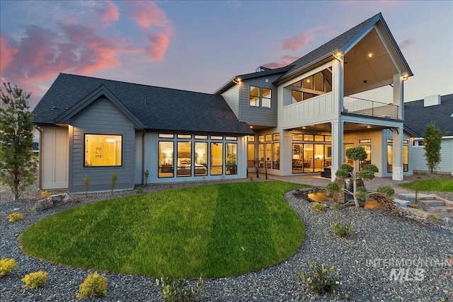 rear view of property featuring a yard, roof with shingles, a balcony, and a patio area