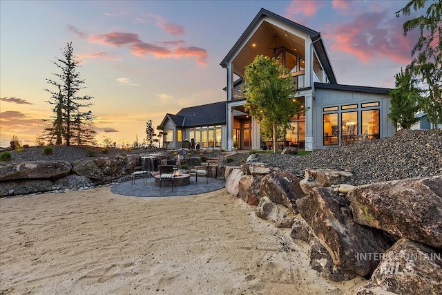 back of property at dusk featuring a patio area, a fire pit, and board and batten siding