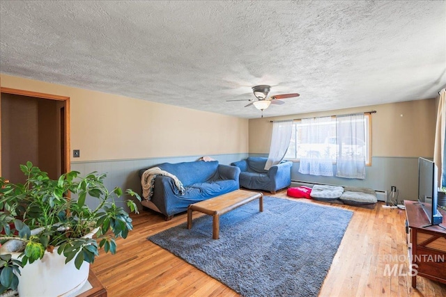 living area with wood finished floors, a textured ceiling, ceiling fan, and a wainscoted wall