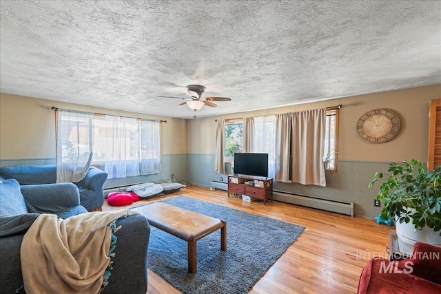 living room featuring a textured ceiling, ceiling fan, a baseboard heating unit, and wood finished floors