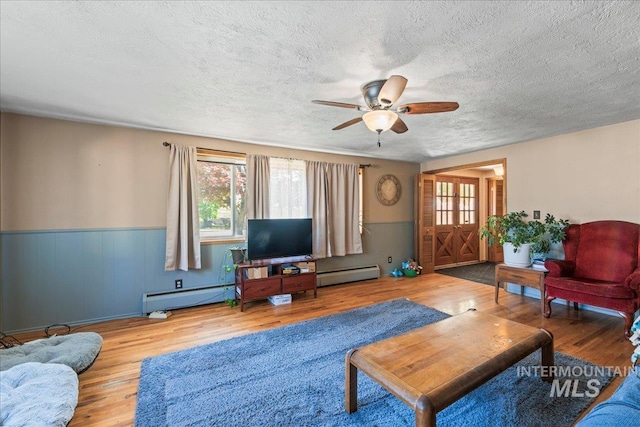 living area with wood finished floors, a baseboard heating unit, and a healthy amount of sunlight