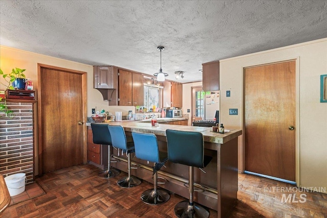 kitchen featuring freestanding refrigerator, a peninsula, a kitchen bar, light countertops, and a textured ceiling