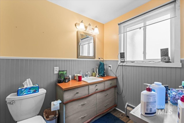 half bath featuring wainscoting, wood finished floors, a healthy amount of sunlight, and toilet
