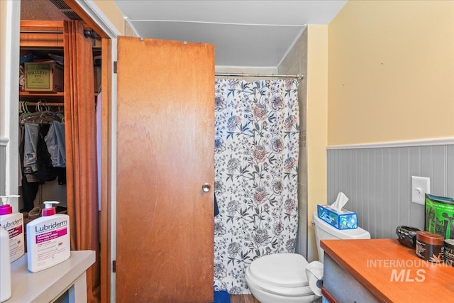 bathroom with toilet, a shower with curtain, and wainscoting