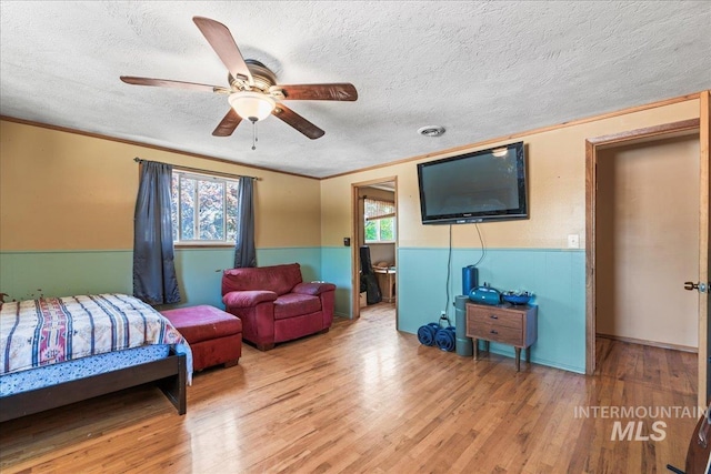 bedroom with crown molding, wainscoting, a textured ceiling, and wood finished floors