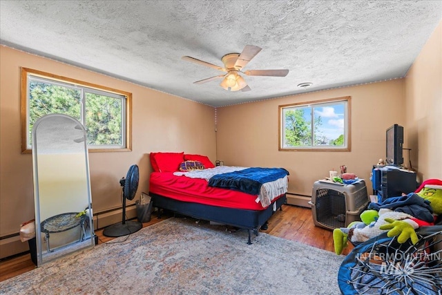 bedroom featuring a textured ceiling, multiple windows, baseboard heating, and wood finished floors