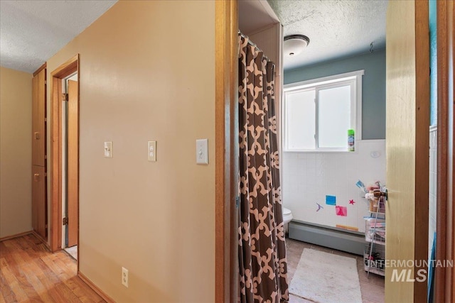 hallway featuring light wood-style floors, a baseboard radiator, and a textured ceiling