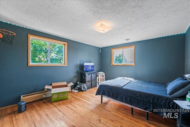 bedroom with baseboards, a textured ceiling, a baseboard heating unit, and wood finished floors