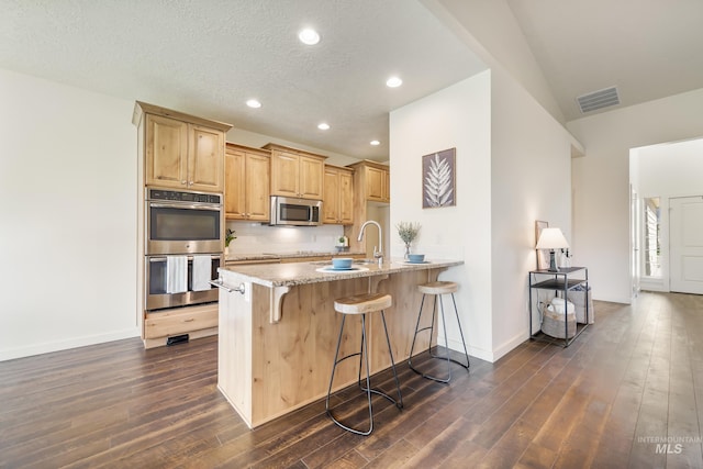 8235 W Tether St, Boise, ID 83709 - kitchen featuring stainless steel appliances, a breakfast bar, dark wood-type flooring, baseboards, and light brown cabinetry