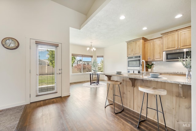 8235 W Tether St, Boise, ID 83709 - kitchen featuring appliances with stainless steel finishes, light brown cabinets, a kitchen breakfast bar, light stone countertops, and tasteful backsplash