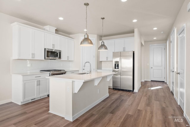 kitchen with a center island with sink, wood finished floors, white cabinets, stainless steel appliances, and a sink