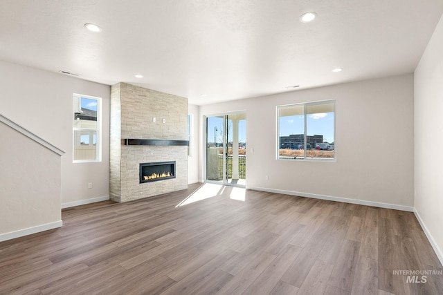 unfurnished living room with a stone fireplace, recessed lighting, wood finished floors, and baseboards