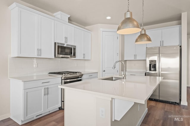 kitchen with an island with sink, appliances with stainless steel finishes, dark wood-style floors, white cabinetry, and a sink