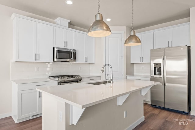 kitchen with dark wood-type flooring, a center island with sink, a sink, white cabinetry, and appliances with stainless steel finishes