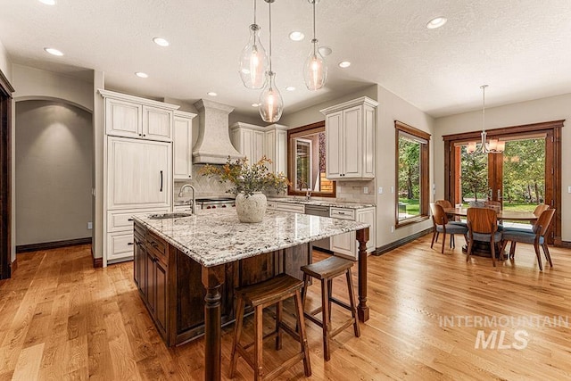 1452 S Hidden Island Pl, Eagle, ID 83616 - kitchen with premium range hood, a chandelier, light stone counters, tasteful backsplash, and a kitchen island with sink