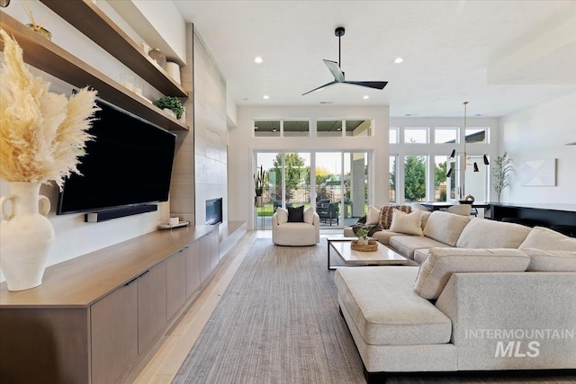 living room with a large fireplace, light hardwood / wood-style floors, and ceiling fan