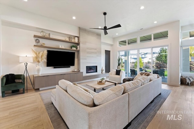 living room featuring ceiling fan, a tiled fireplace, and light hardwood / wood-style flooring