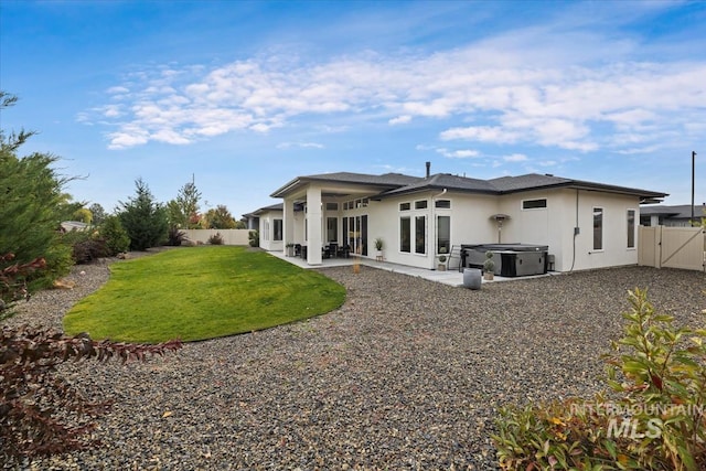 rear view of house featuring a hot tub, a patio, and a yard