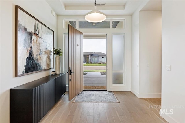 foyer entrance with light hardwood / wood-style floors and a raised ceiling