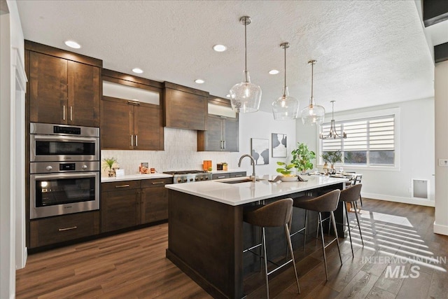 kitchen featuring sink, dark brown cabinets, an island with sink, a kitchen bar, and stainless steel double oven