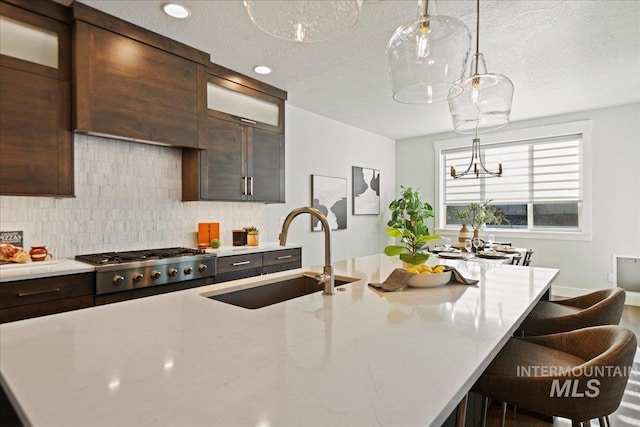 kitchen featuring sink, a center island with sink, backsplash, and dark brown cabinetry