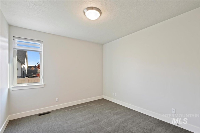 spare room with a textured ceiling and dark colored carpet