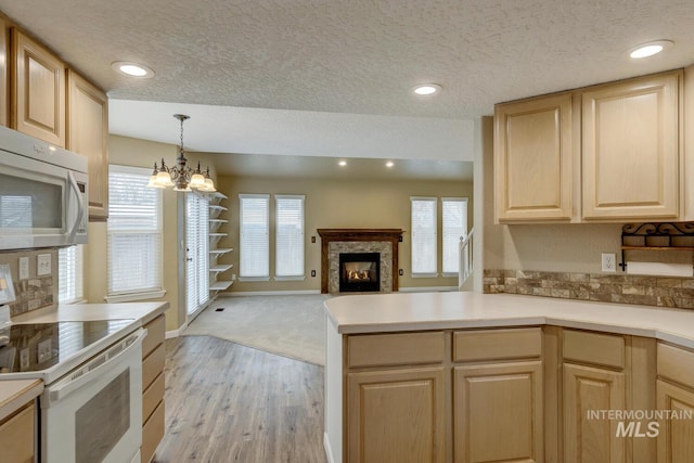 kitchen with hanging light fixtures, an inviting chandelier, kitchen peninsula, white appliances, and light brown cabinetry