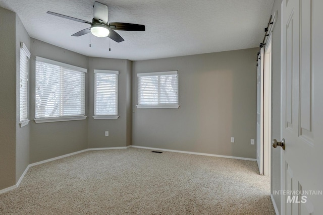 carpeted spare room featuring a barn door, ceiling fan, and a textured ceiling