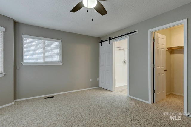 unfurnished bedroom featuring light carpet, a walk in closet, ceiling fan, a barn door, and a closet