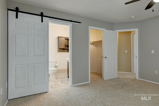 unfurnished bedroom featuring a walk in closet, ceiling fan, a barn door, connected bathroom, and a closet