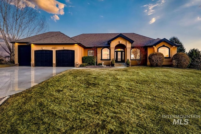 view of front of property featuring stone siding, an attached garage, concrete driveway, and a yard